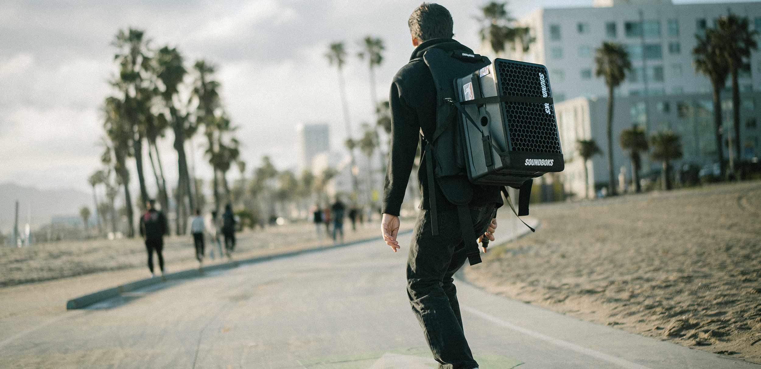 A person riding a skateboard with a SOUNDBOKS Go strapped to his back with THE BACKPACK