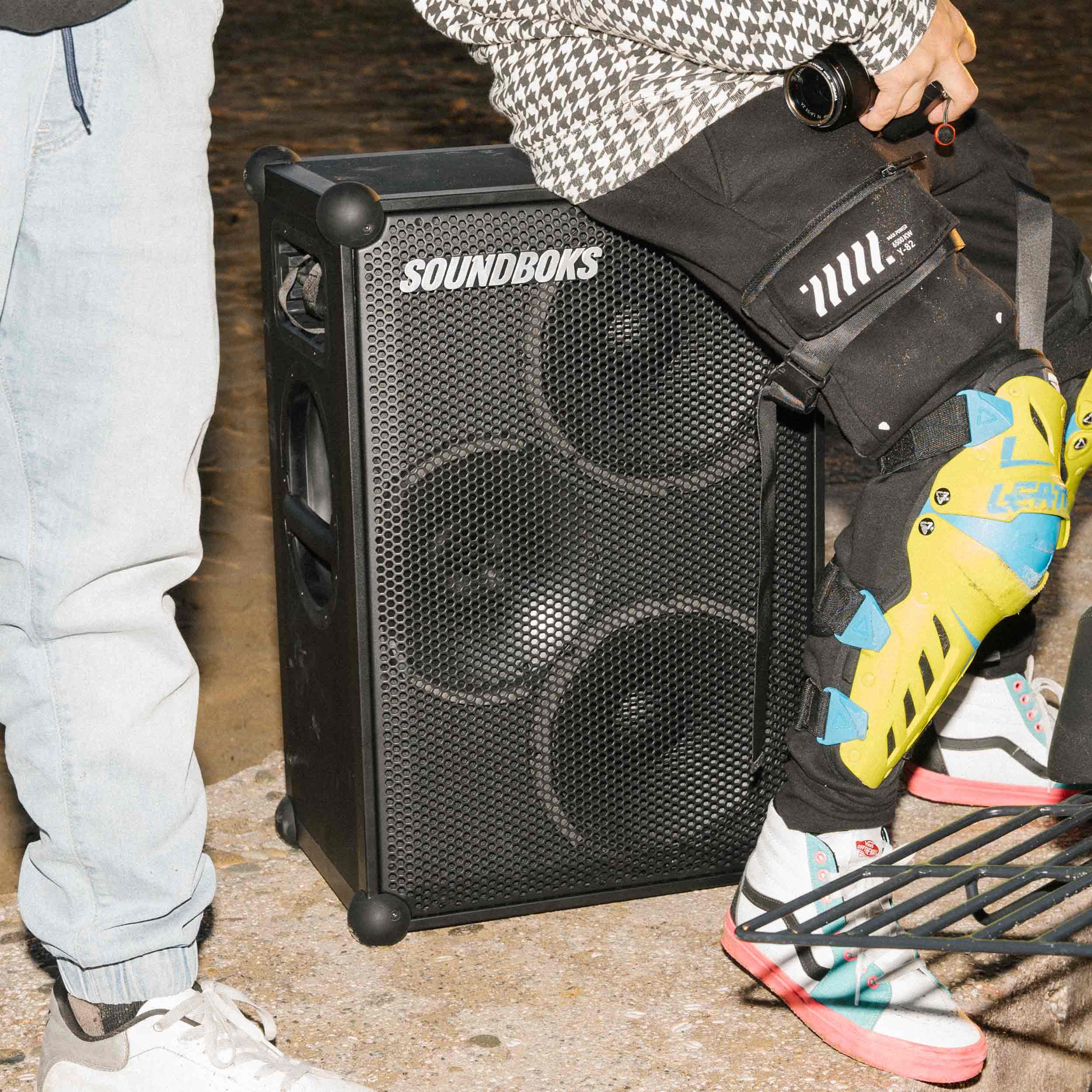 A person sits on a SOUNDBOKS 4 party speaker outsdoors